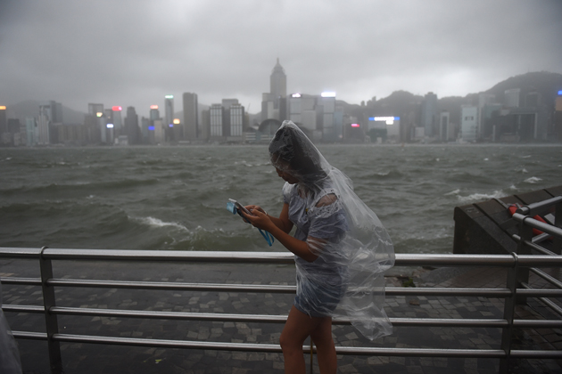 A woman uses her phone while wearing a plastic poncho along Victoria Harbour during heavy winds and rain brought on by Typhoon Hato in Hong Kong on August 23, 2017. Typhoon Hato smashed into Hong Kong on August 23 with hurricane force winds and heavy rains in the worst storm the city has seen for five years, shutting down the stock market and forcing the cancellation of hundreds of flights. / AFP PHOTO / Anthony WALLACE