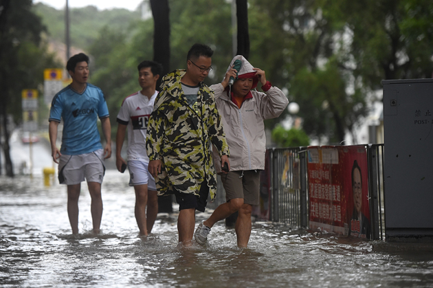 Pedestrians walk through floodwaters along a street after heavy rains brought on by Typhoon Hato in Hong Kong on August 23, 2017. Typhoon Hato smashed into Hong Kong on August 23 with hurricane force winds and heavy rains in the worst storm the city has seen for five years, shutting down the stock market and forcing the cancellation of hundreds of flights. / AFP PHOTO / Anthony WALLACE