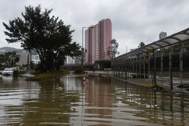 A man (back C) walks past a flooded bus stop after heavy rains brought on by Typhoon Hato in Hong Kong on August 23, 2017. Typhoon Hato left three dead in the gambling hub of Macau on August 23 as it brought chaos and destruction to the enclave after sweeping through neighbouring Hong Kong, where one man also died. / AFP PHOTO / Anthony WALLACE