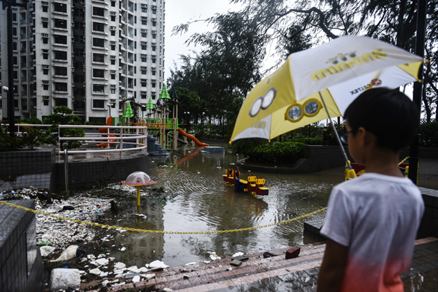 A young child looks at a flooded playground and marine debris after heavy winds and rains brought on by Typhoon Hato in Hong Kong on August 23, 2017. Typhoon Hato left three dead in the gambling hub of Macau on August 23 as it brought chaos and destruction to the enclave after sweeping through neighbouring Hong Kong, where one man also died. / AFP PHOTO / Anthony WALLACE