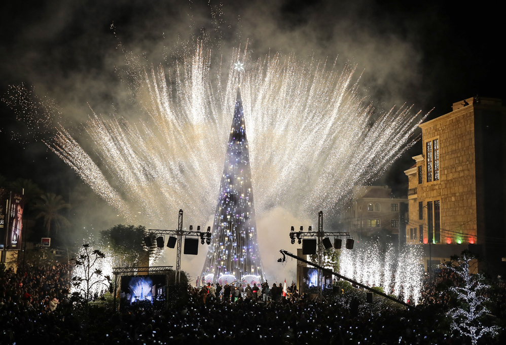 People gather and use their cell phones to film fireworks as they light the sky during the lighting of a Christmas tree in a square in the Lebanese coastal city of Byblos, north of Beirut, on November 30, 2017. / AFP PHOTO / JOSEPH EID