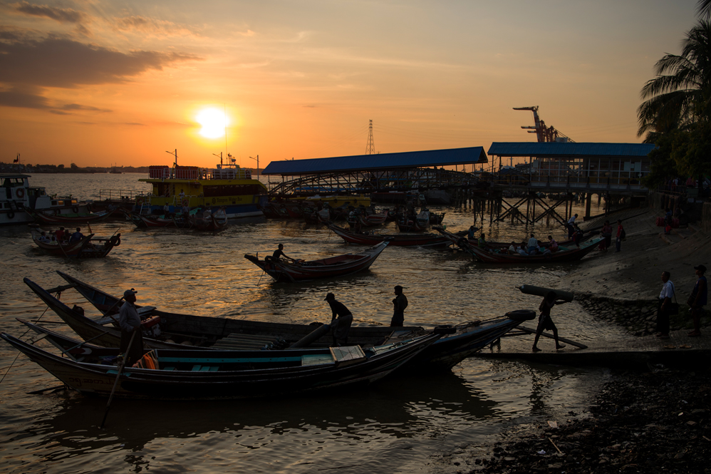 This photo taken on December 1, 2017 shows a labourer (bottom R) unloading goods from a boat during sunset at the Yangon jetty. / AFP PHOTO / YE AUNG THU