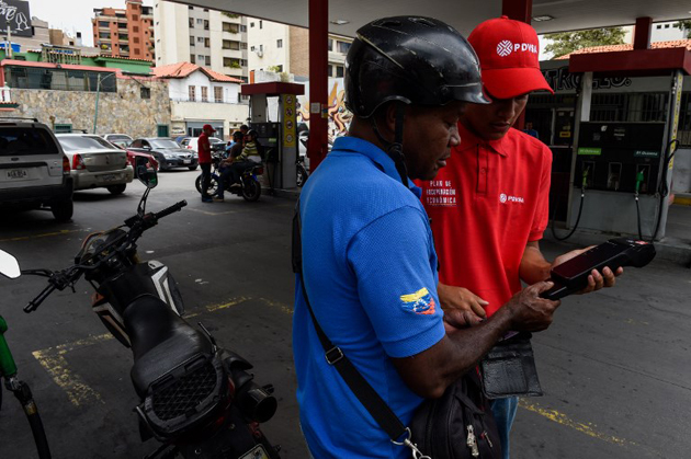 A volunteer explains a customer how the new gas payment system which requires the "Fatherland's Card" works, at a gas station in Caracas, on September 20, 2018 as Venezuela tests the system nationwide. In August, President Nicolas Maduro announced that Venezuela's dirt-cheap fuel would be available only to people with the so-called "carnet de la patria," or fatherland card, which provides access to government assistance and that the opposition had denounced as a tool for controlling people. / AFP PHOTO / Federico PARRA