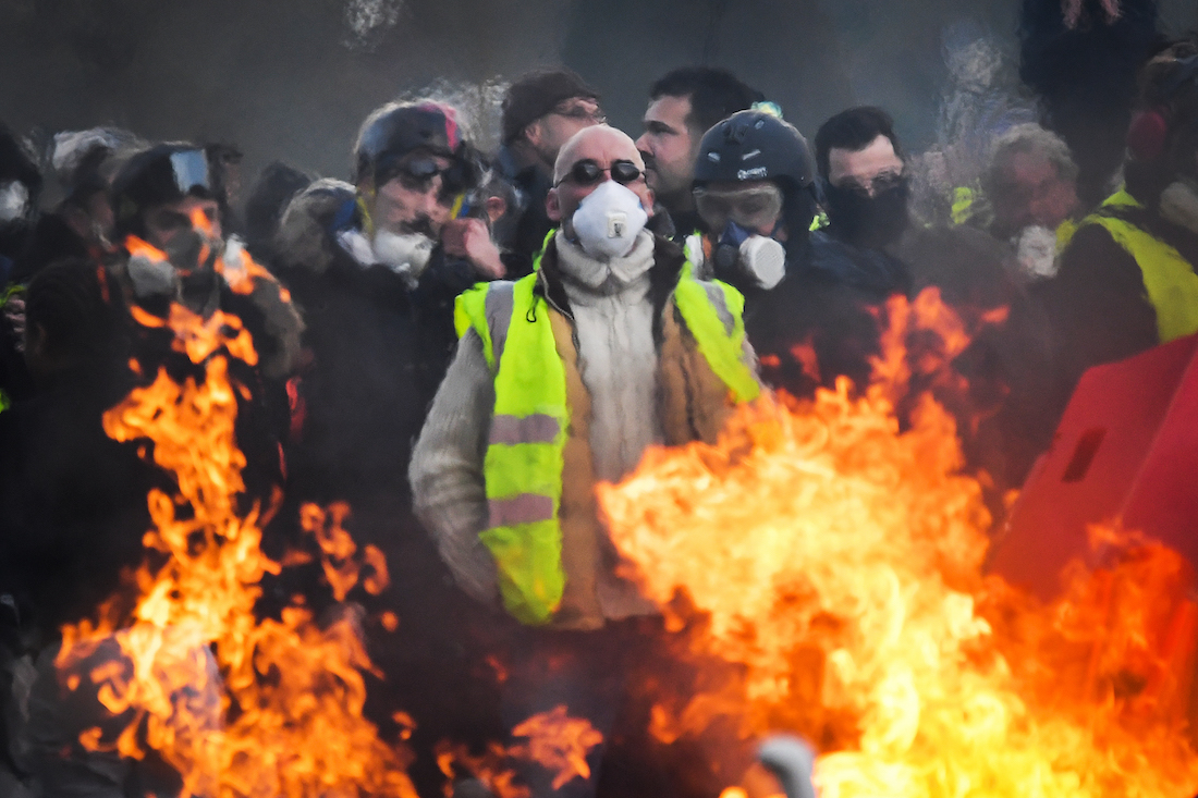 Protesters stand behind a barricade set on fire during an anti-government demonstration called by the "yellow vests" (gilets jaunes) movement on January 19, 2019, in Angers, western France. - France's "yellow vests" took to the streets on January 19 for a 10th straight weekend of anti-government protests, despite attempts by the president to channel their anger into a series of town hall debates. (Photo by LOIC VENANCE / AFP)