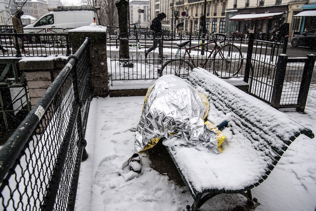 A homeless man sleeps under blankets on a bench as snow falls over in Paris on January 22, 2019. (Photo by Christophe ARCHAMBAULT / AFP)