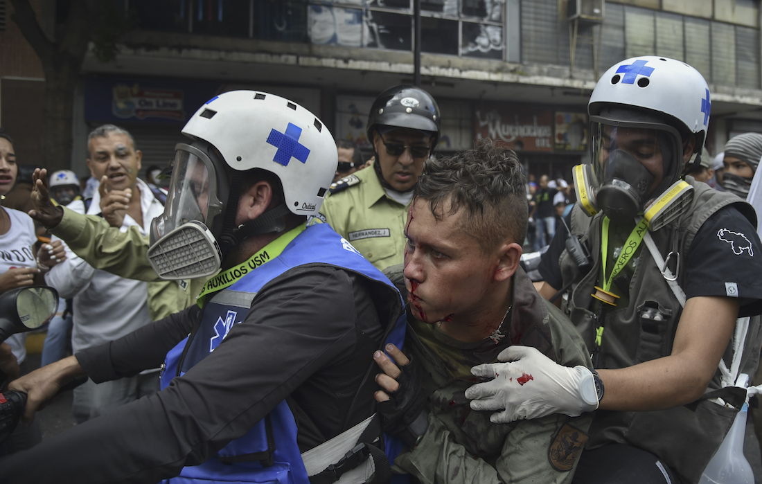 Paramedics rescue a wounded member of the Bolivarian National Guard during clashes with opposition demonstrators, in a protest against the government of President Nicolas Maduro on the anniversary of the 1958 uprising that overthrew the military dictatorship, in Caracas on January 23, 2019. - Venezuela's National Assembly head Juan Guaido declared himself the country's "acting president" on Wednesday during a mass opposition rally against leader Nicolas Maduro. (Photo by YURI CORTEZ / AFP)