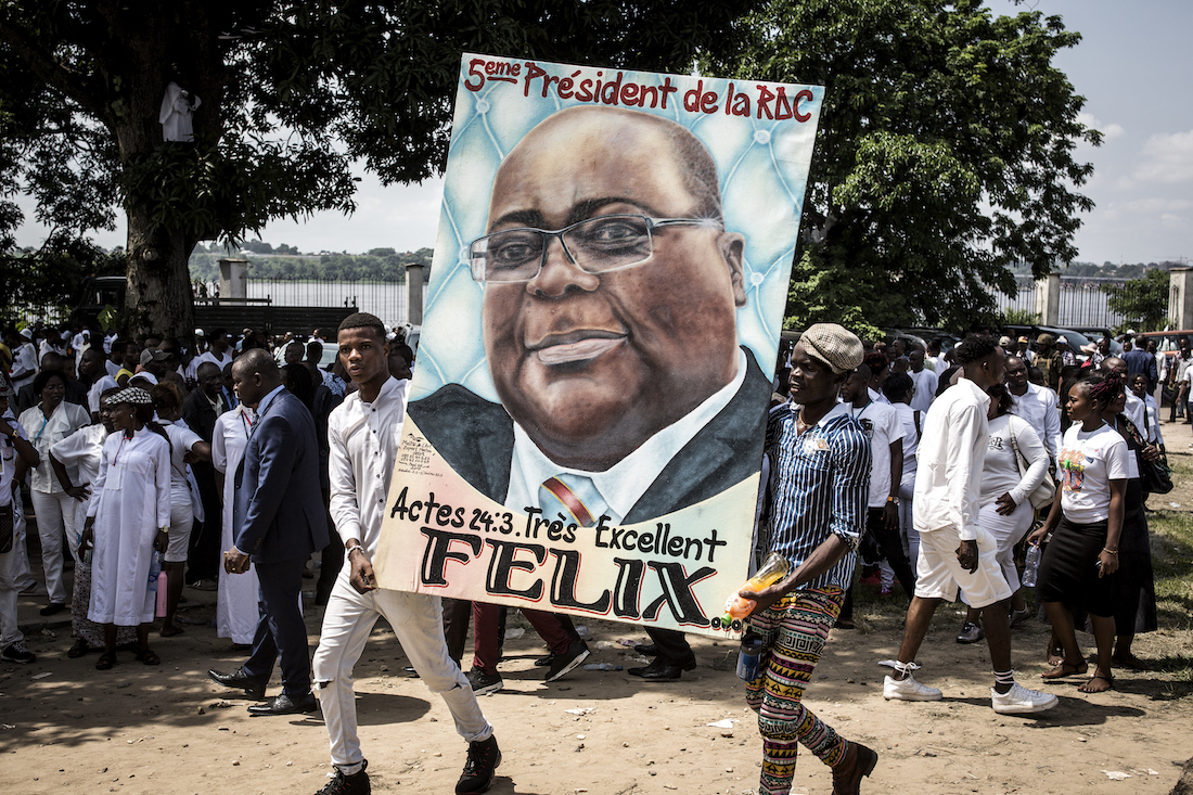 Supporters of new elected President of the Democratic Republic of Congo Felix Tshisekedi hold his portrait and cheer during his Presidential Inauguration on January 24, 2018 in Kinshasa. - Tshisekedi took the oath of office before receiving the national flag and a copy of the constitution from outgoing president Joseph Kabila, stepping aside after 18 years at the helm of sub-Saharan Africa's biggest country, marking the country's first-ever peaceful handover of power after chaotic and bitterly-disputed elections. (Photo by John WESSELS / AFP)