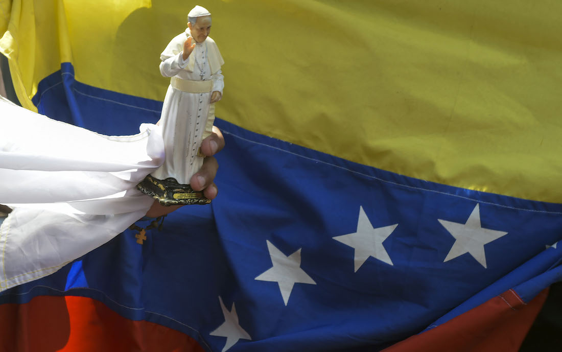 A faithful holds a souvenir doll of Pope Francis next to a Venezuelan national flag, while gathering alongside the street to see him, during the World Youth Days in Panama City on January 24, 2019. - Pope Francis will on Thursday formally open World Youth Day celebrations which have drawn around 200,000 young people from around the world to Panama where he is expected to defend Central American migrants and human rights. (Photo by Raul Arboleda / AFP)