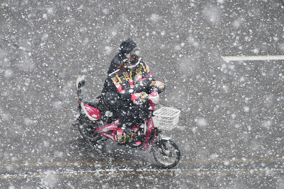 A resident rides an electric bicycle during a snowfall in Yantai in China's eastern Shandong province on December 4, 2017.  An orange alert of road icing was issued by local meteorological bureau on December 4. / AFP PHOTO / - / China OUT