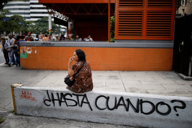 A woman waits for transportation next to a graffiti that reads "How much longer?" in front of a closed metro station during a blackout in Caracas, Venezuela July 31, 2018. REUTERS/Carlos Garcia Rawlins